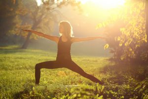 Young woman practicing yoga in nature (virabhadrasana position). About 20 years old, Caucasian blonde in sports clothing stretching.
